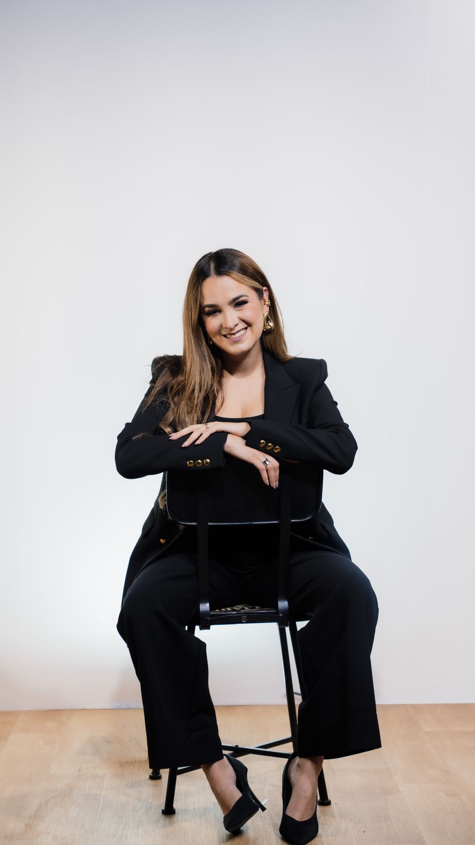 Michelle Ruiz, de traje sastre negro, sentada de cuerpo entero en un banco alto.